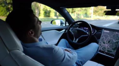 Kentsel yolda kendi kendini kullanan bir erkek işadamı deneyimi. Şehirdeki otomatik pilotla elektrikli otomobilde dinlenen kendine güvenen bir iş adamı. Yavaş çekim