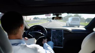 Erkek işadamı, şehir yolunda otomatik pilotla elektrikli araca binerken kitap okuyor. Başarılı bir iş adamı, kendi başına elektrikli araba sürerken bilgisini geliştiriyor..