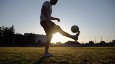 Sporcunun silueti gün batımında sahada topla numara yapıyor. Çayır 'da üniformalı profesyonel erkek futbolcu. Arka planda güneş ışığı var. Serbest stil futbol kavramı.