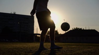 Yeşil sahada topa vuran genç adam bacakları. Günbatımında stadyumda futbol oynayan erkek futbolcu. Sporcu dışarıda numaralar yapıyor. Serbest stil futbol kavramı.