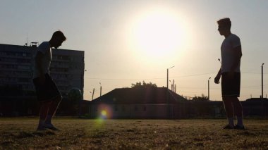 Günbatımında stadyumda futbol oynayan profesyonel futbolcuların silueti. Sahada birbirlerine pas verirken iki sporcu topla numara yapıyor. Serbest stil futbol.