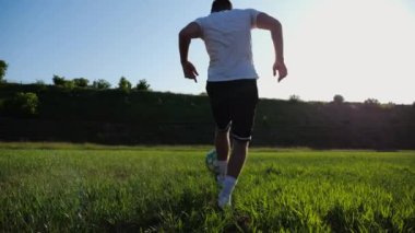 Güneşli bir günde stadyumda futbol topuyla hokkabazlık yapan sporcu. Genç adam yeşil sahada topa vuruyor. Profesyonel futbolcu, arka planda güneş ışığıyla çayırda numaralar yapıyor. Serbest stil futbol.