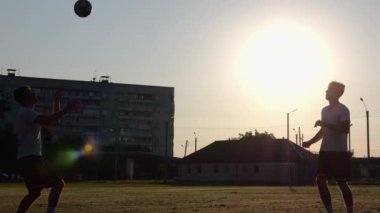 Günbatımında stadyumda futbol oynayan profesyonel futbolcuların silueti. Sahada birbirlerine pas verirken iki sporcu topla numara yapıyor. Serbest stil futbol.