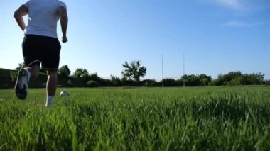 Üniformalı profesyonel futbolcu yeşil sahada koşarken topa numara yapıyor. Sporcu güneşli bir günde Meadow 'da koşarken topa vurur. Stadyumda antrenman yapan genç adam. Serbest stil futbol.