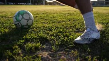 Profesyonel futbolcunun erkek ayağı, yeşil sahada koşarken topla numaralar gösterir. Sporcu bacakları gün batımında çayırda koşarken topa vurur. Stadyumda antrenman yapan genç adam. Yavaş çekim