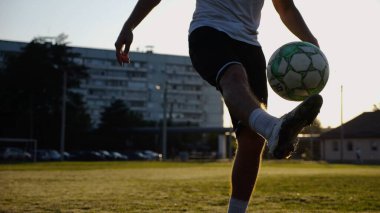 Yeşil sahada topa vuran genç adam bacakları. Günbatımında stadyumda futbol oynayan erkek futbolcu. Sporcu dışarıda numaralar yapıyor. Serbest stil futbol kavramı.