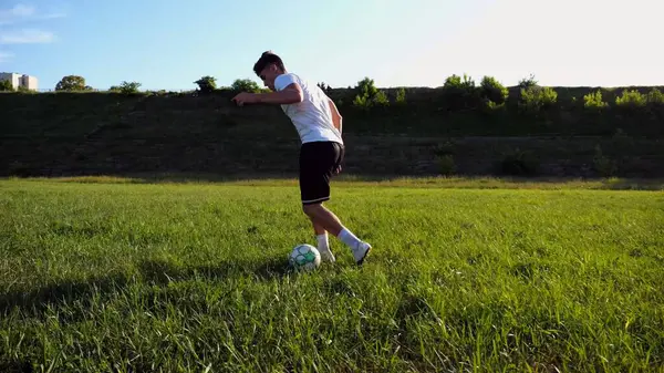 Üniformalı profesyonel futbolcu yeşil sahada koşarken topa numara yapıyor. Sporcu güneşli bir günde Meadow 'da koşarken topa vurur. Stadyumda antrenman yapan genç adam. Serbest stil futbol.