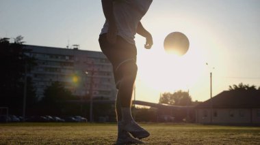 Yeşil sahada topa vuran genç adam bacakları. Günbatımında stadyumda futbol oynayan erkek futbolcu. Sporcu dışarıda numaralar yapıyor. Serbest stil futbol kavramı.