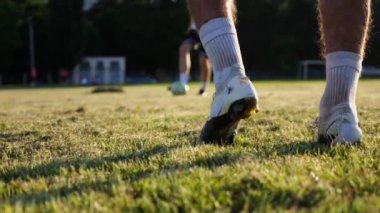 Günbatımında stadyumda futbol topu atan profesyonel futbolcuların erkek ayakları. Yeşil sahada topa vuran sporcu bacakları. Genç adamlar Meadow 'da antrenman yapıyor. Serbest stil futbol kavramı. Yavaş