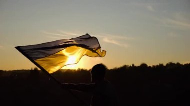 Askeri üniformalı genç adam arka planda güzel günbatımına karşı Ukrayna bayrağı sallıyor. Erkek Ukraynalı asker kırsal kesimde ulusal bayrağı kaldırdı. Rus saldırısına karşı zafer.