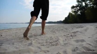 Sahilde arka planda deniz manzarasıyla koşan çıplak ayaklı bir kadın. Deniz kıyısında koşan dişi bacaklar. Mutlu bayan okyanus kıyısında vakit geçiriyor. Yaz tatili kavramı.