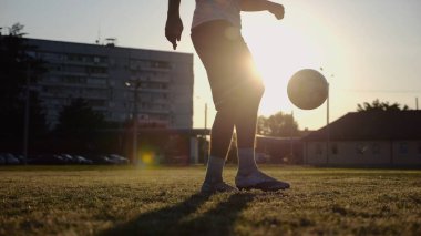 Yeşil sahada topa vuran genç adam bacakları. Günbatımında stadyumda futbol oynayan erkek futbolcu. Sporcu dışarıda numaralar yapıyor. Serbest stil futbol kavramı.
