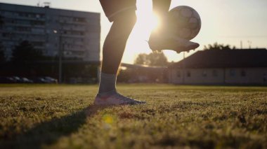 Yeşil sahada topa vuran genç adam bacakları. Günbatımında stadyumda futbol oynayan erkek futbolcu. Sporcu dışarıda numaralar yapıyor. Serbest stil futbol kavramı.