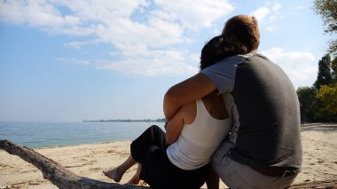 Sahilde tahta kütüğün üzerinde otururken romantik bir çift kucaklaşması. Denize ve manzaraya hayran olan mutlu bir çift. Sevgililer tatil köyünde birlikte vakit geçirirler. Tatil ya da tatil kavramı. Yavaş çekim