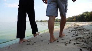 Çıplak ayaklı bir çift okyanus arka planında plaj boyunca birlikte yürüyorlar. Denize yakın yürüyen erkek ve dişi bacaklar. Kumlu sahilde mutlu aşıklar. Yaz tatili veya tatil kavramı.