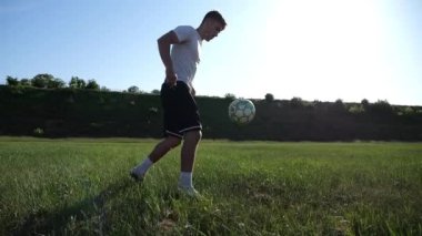 Güneşli bir günde stadyumda futbol topuyla hokkabazlık yapan sporcu. Genç adam yeşil sahada topa vuruyor. Profesyonel futbolcu, arka planda güneş ışığıyla çayırda numaralar yapıyor. Serbest stil futbol.
