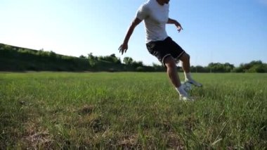 Üniformalı profesyonel futbolcu yeşil sahada koşarken topa numara yapıyor. Sporcu güneşli bir günde Meadow 'da koşarken topa vurur. Stadyumda antrenman yapan genç adam. Serbest stil futbol.
