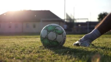 Erkek futbolcu gün batımında stadyumda penaltı atışı yapıyor. Yeşil sahada topa vuran sporcu bacağı. Genç adam Meadow 'da eğitim görüyor. Serbest stil futbol kavramı. Yavaş