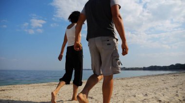 El ele tutuşup sahilde yürüyen bir çift. Güneşli bir günde deniz kıyısına giden mutlu bir çift. Sevgililer tatil köyünde birlikte vakit geçirirler. Tatil ya da tatil kavramı.