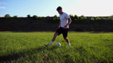 Üniformalı profesyonel futbolcu yeşil sahada koşarken topa numara yapıyor. Sporcu güneşli bir günde Meadow 'da koşarken topa vurur. Stadyumda antrenman yapan genç adam. Serbest stil futbol.