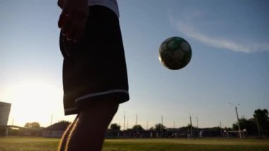 Yeşil sahada topa vuran genç adam bacakları. Günbatımında stadyumda futbol oynayan erkek futbolcu. Sporcu dışarıda numaralar yapıyor. Serbest stil futbol kavramı.