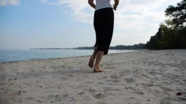 Sahilde arka planda deniz manzarasıyla koşan çıplak ayaklı bir kadın. Deniz kıyısında koşan dişi bacaklar. Mutlu bayan okyanus kıyısında vakit geçiriyor. Yaz tatili kavramı.