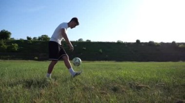 Güneşli bir günde stadyumda futbol topuyla hokkabazlık yapan sporcu. Genç adam yeşil sahada topa vuruyor. Profesyonel futbolcu, arka planda güneş ışığıyla çayırda numaralar yapıyor. Serbest stil futbol.