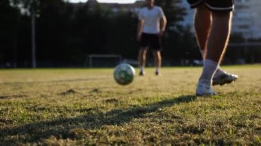 Günbatımında stadyumda futbol topu atan profesyonel futbolcuların erkek ayakları. Yeşil sahada topa vuran sporcu bacakları. Genç adamlar Meadow 'da antrenman yapıyor. Serbest stil futbol kavramı. Yavaş