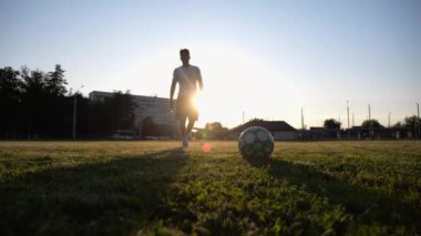 Sporcunun silueti gün batımında stadyuma penaltı atışı yapıyor. Profesyonel futbolcu yeşil sahada futbol topunu tekmeliyor. Genç adam Meadow 'da eğitim görüyor. Serbest stil futbol kavramı.