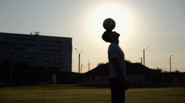 Sporcunun silueti gün batımında sahada topla numara yapıyor. Çayır 'da üniformalı profesyonel erkek futbolcu. Arka planda güneş ışığı var. Serbest stil futbol kavramı.