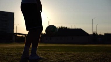Yeşil sahada topa vuran genç adam bacakları. Günbatımında stadyumda futbol oynayan erkek futbolcu. Sporcu dışarıda numaralar yapıyor. Serbest stil futbol kavramı.