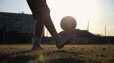Yeşil sahada topa vuran genç adam bacakları. Günbatımında stadyumda futbol oynayan erkek futbolcu. Sporcu dışarıda numaralar yapıyor. Serbest stil futbol kavramı.