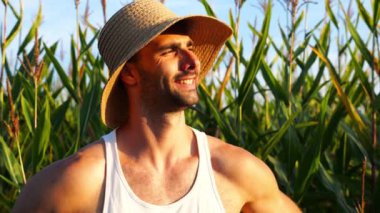 Mutlu gülümseyen erkek çiftçi mısır çayırının yanında kameraya bakar. Arkaplanda mısır tarlası olan hasır şapkalı genç ve yakışıklı tarımcı portresi. Tarım sektörü kavramı