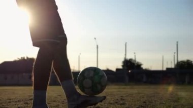 Yeşil sahada topa vuran genç adam bacakları. Günbatımında stadyumda futbol oynayan erkek futbolcu. Sporcu dışarıda numaralar yapıyor. Serbest stil futbol kavramı.