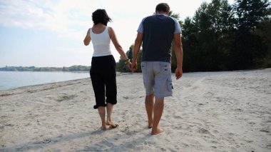 El ele tutuşup sahilde yürüyen bir çift. Güneşli bir günde deniz kıyısına giden mutlu bir çift. Sevgililer tatil köyünde birlikte vakit geçirirler. Tatil ya da tatil kavramı.