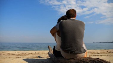 Sahilde tahta kütüğün üzerinde otururken romantik bir çift kucaklaşması. Denize ve manzaraya hayran olan mutlu bir çift. Sevgililer tatil köyünde birlikte vakit geçirirler. Tatil ya da tatil kavramı. Yavaş çekim