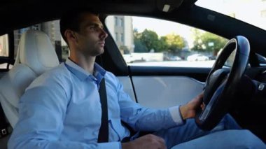 Şehir yolunda modern elektrikli araba kullanan yakışıklı bir işadamının profili. Erkek başarılı girişimci şehirde elektrikli araçla geziyor. Genç adam güneşli bir günde işe gidip geliyor. Yavaş çekim