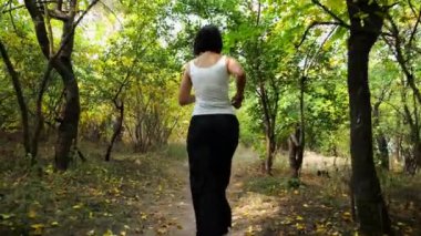 Yetişkin esmer kadın yaz ormanlarında yol boyunca koşuyor. Vahşi doğada koşan bir kadın. Tanınmayan bir kadın güzel manzarada vakit geçiriyor. Yavaşla.