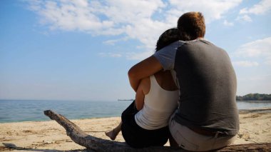 Sahilde tahta kütüğün üzerinde otururken romantik bir çift kucaklaşması. Denize ve manzaraya hayran olan mutlu bir çift. Sevgililer tatil köyünde birlikte vakit geçirirler. Tatil ya da tatil kavramı. Yavaş çekim