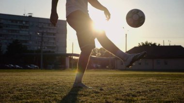 Yeşil sahada topa vuran genç adam bacakları. Günbatımında stadyumda futbol oynayan erkek futbolcu. Sporcu dışarıda numaralar yapıyor. Serbest stil futbol kavramı.