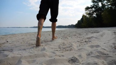Sahilde arka planda deniz manzarasıyla koşan çıplak ayaklı bir kadın. Deniz kıyısında koşan dişi bacaklar. Mutlu bayan okyanus kıyısında vakit geçiriyor. Yaz tatili kavramı.