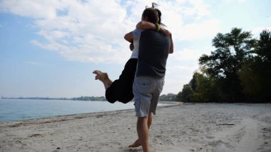 El ele tutuşup sahilde yürüyen bir çift. Adam kadını havaya uçurup kıyı şeridinde geri dönüyor. Mutlu çift yaz tatilinde deniz kıyısında birlikte eğleniyor. Aşk kavramı.