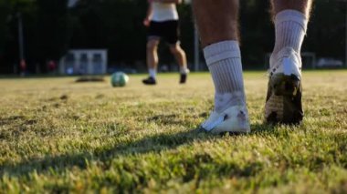 Günbatımında stadyumda futbol topu atan profesyonel futbolcuların erkek ayakları. Yeşil sahada topa vuran sporcu bacakları. Genç adamlar Meadow 'da antrenman yapıyor. Serbest stil futbol kavramı. Yavaş