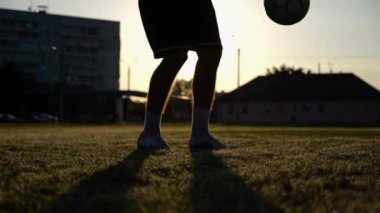 Yeşil sahada topa vuran genç adam bacakları. Günbatımında stadyumda futbol oynayan erkek futbolcu. Sporcu dışarıda numaralar yapıyor. Serbest stil futbol kavramı.