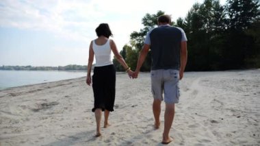 El ele tutuşup sahilde yürüyen bir çift. Güneşli bir günde deniz kıyısına giden mutlu bir çift. Sevgililer tatil köyünde birlikte vakit geçirirler. Tatil ya da tatil kavramı. Yavaş çekim