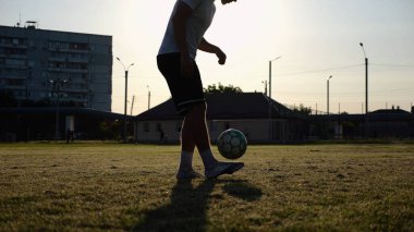 Yeşil sahada topa vuran genç adam bacakları. Günbatımında stadyumda futbol oynayan erkek futbolcu. Sporcu dışarıda numaralar yapıyor. Serbest stil futbol kavramı.