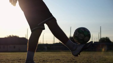 Yeşil sahada topa vuran genç adam bacakları. Günbatımında stadyumda futbol oynayan erkek futbolcu. Sporcu dışarıda numaralar yapıyor. Serbest stil futbol kavramı.
