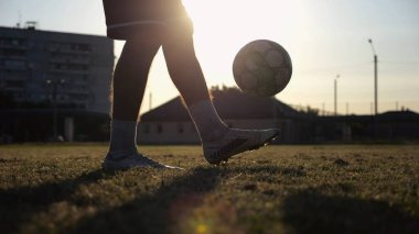Yeşil sahada topa vuran genç adam bacakları. Günbatımında stadyumda futbol oynayan erkek futbolcu. Sporcu dışarıda numaralar yapıyor. Serbest stil futbol kavramı.