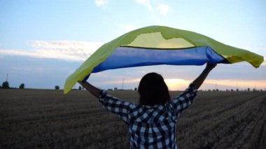 Ukraynalı kadın gün doğumunda ulusal mavi-sarı bayrak ile arpa çayırında koşuyor. Gün batımında kafasının üstünde Ukrayna bayrağıyla koşan bir kadın. Rus saldırısına karşı zafer.