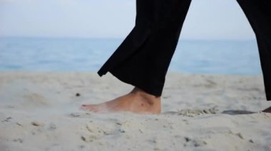 Sahilde kumsalda arka planda deniz manzarası olan kadın ayakları. Deniz kıyısında yürüyen yetişkin kadın bacakları. Çıplak ayaklı kadın okyanus kıyısında geziniyor. Yaz tatili kavramı.
